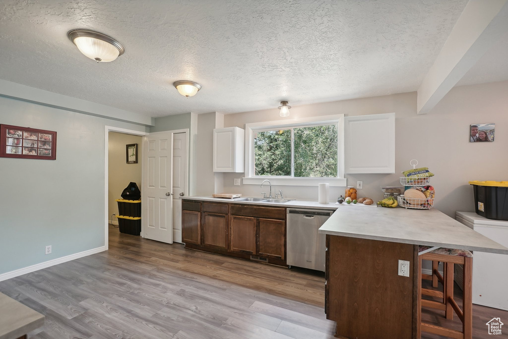 Kitchen featuring stainless steel dishwasher, sink, a kitchen bar, light hardwood / wood-style floors, and a textured ceiling