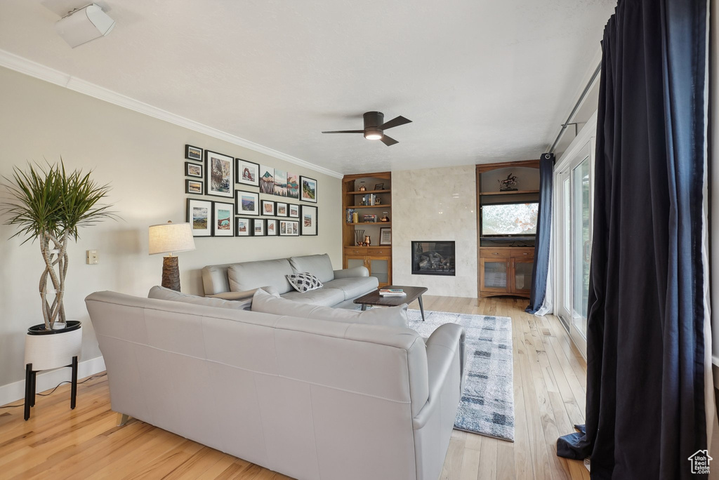 Living room with built in features, ceiling fan, light wood-type flooring, and crown molding