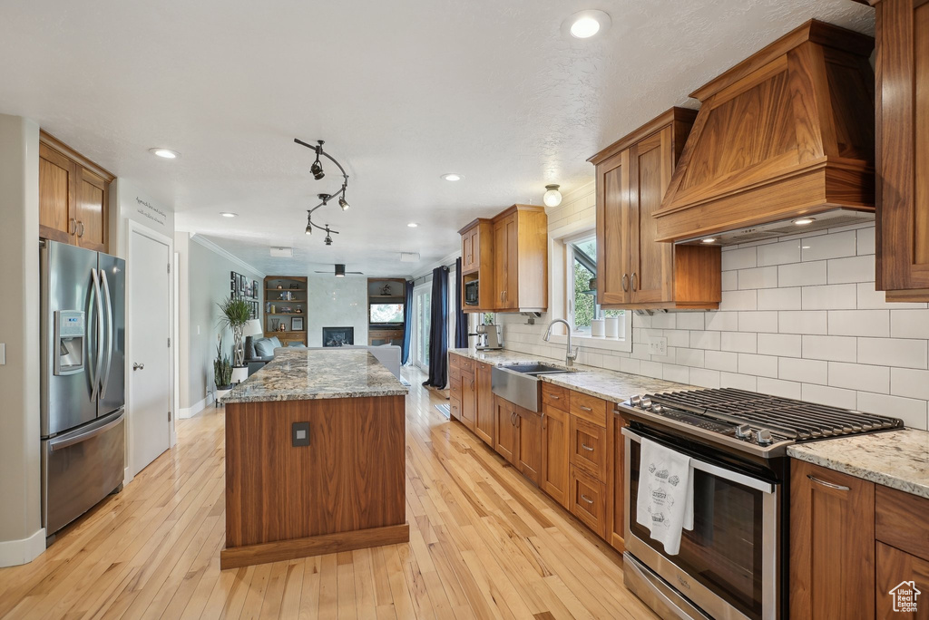 Kitchen with premium range hood, light wood-type flooring, a kitchen island, appliances with stainless steel finishes, and backsplash