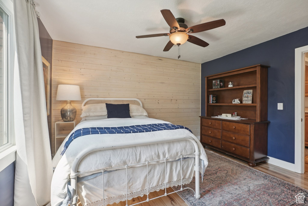 Bedroom with wood walls, ceiling fan, and hardwood / wood-style floors