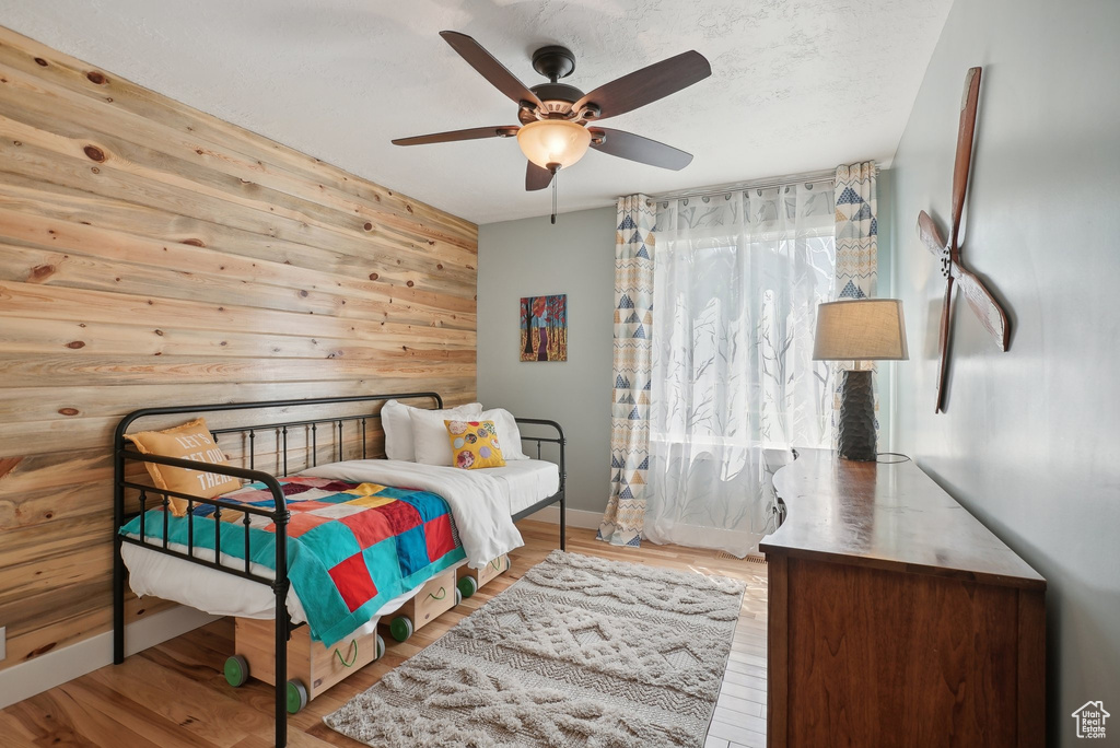 Bedroom with wood walls, light wood-type flooring, and ceiling fan