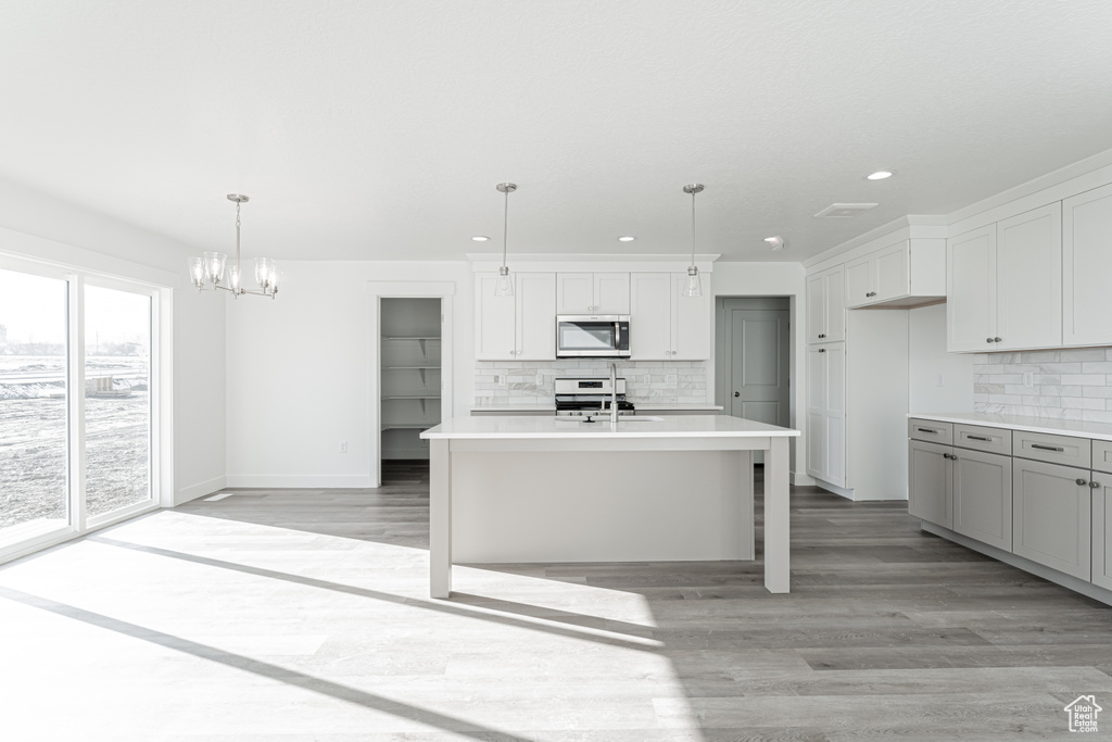 Kitchen featuring backsplash, white cabinetry, an island with sink, and hanging light fixtures
