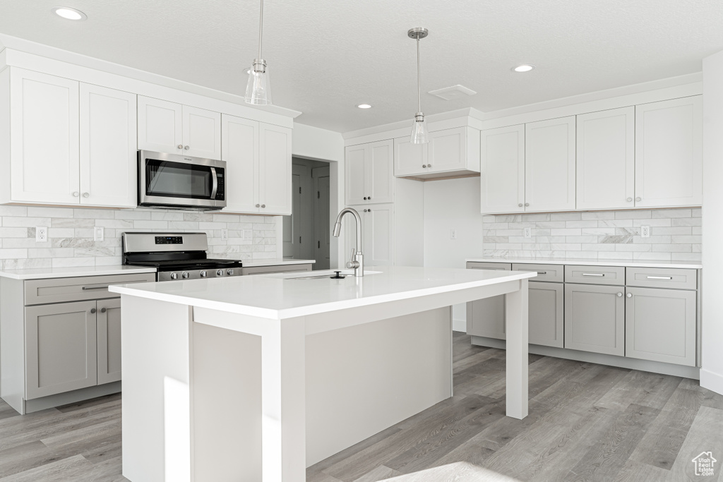 Kitchen with pendant lighting, sink, stainless steel appliances, and a kitchen island with sink