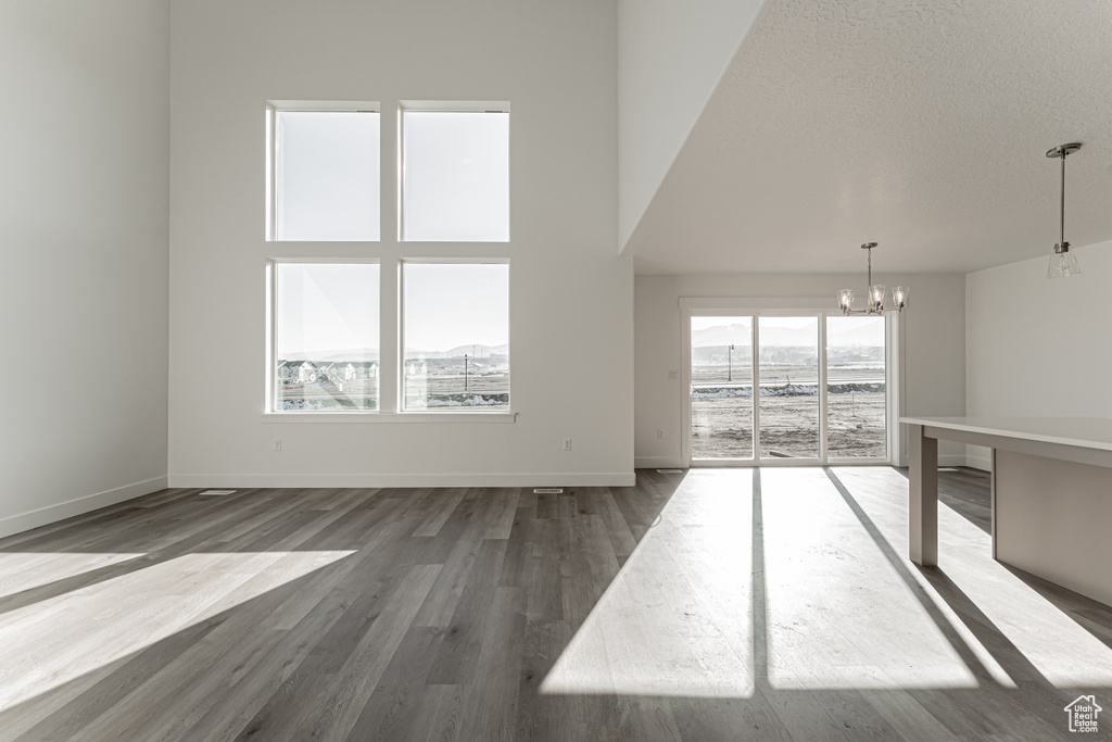 Unfurnished living room featuring a notable chandelier, dark hardwood / wood-style floors, a towering ceiling, and a textured ceiling