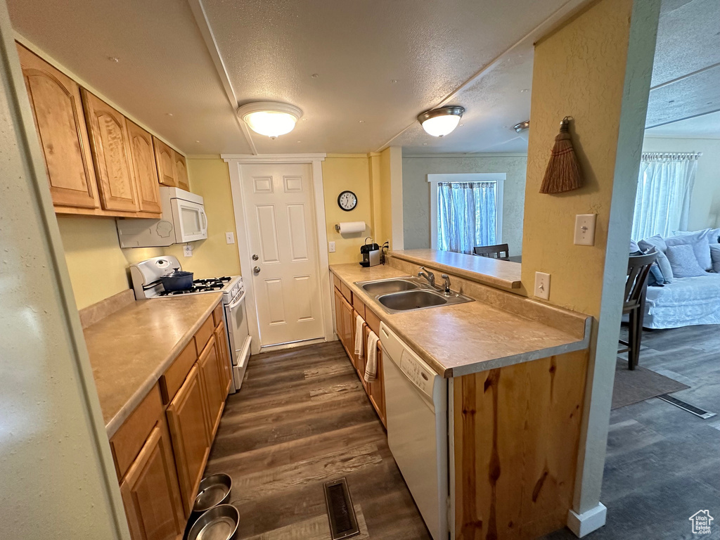 Kitchen featuring white appliances, sink, kitchen peninsula, a textured ceiling, and dark wood-type flooring