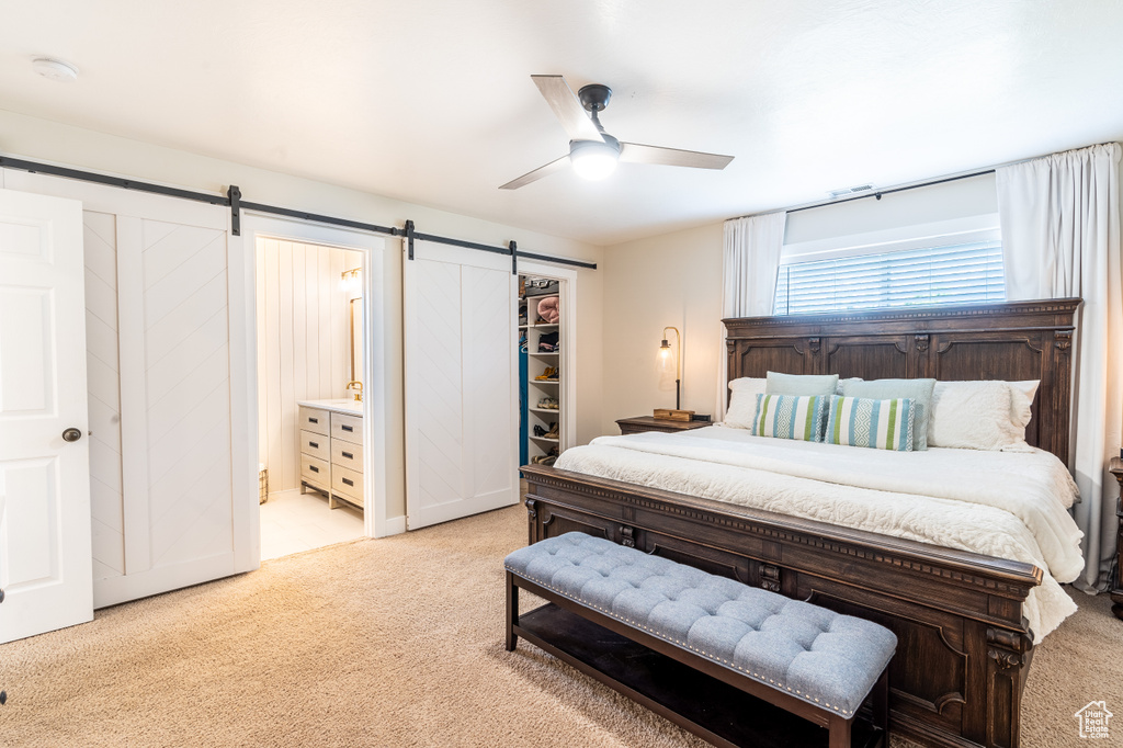 Bedroom featuring a barn door, ceiling fan, ensuite bathroom, light carpet, and a closet