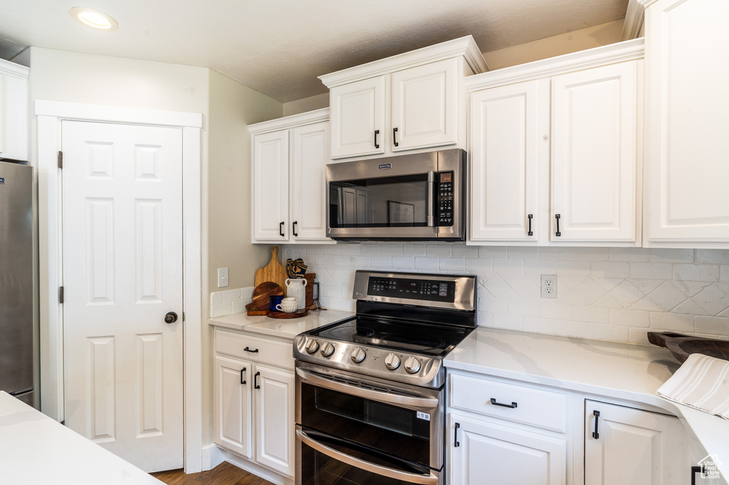 Kitchen with white cabinetry, backsplash, stainless steel appliances, light stone countertops, and wood-type flooring