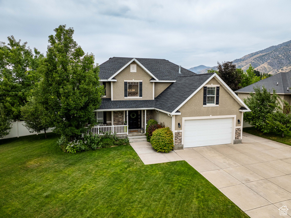 View of front of house featuring a mountain view, a porch, a garage, and a front lawn