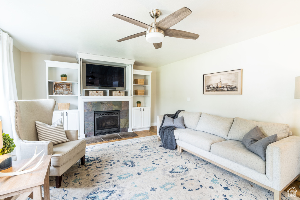 Living room with a tiled fireplace, light wood-type flooring, and ceiling fan