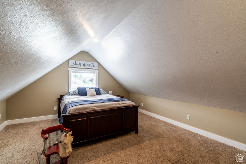 Bedroom with light carpet, vaulted ceiling, and a textured ceiling