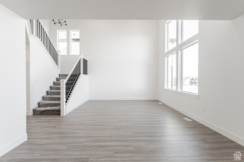 Unfurnished living room featuring wood-type flooring, a textured ceiling, and a notable chandelier