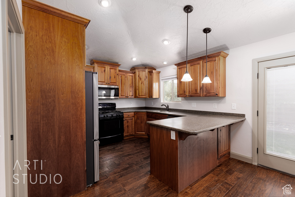 Kitchen with pendant lighting, dark hardwood / wood-style flooring, kitchen peninsula, and stainless steel appliances