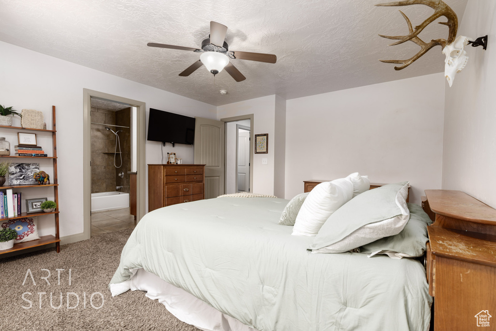 Carpeted bedroom featuring a closet, ensuite bath, a textured ceiling, a walk in closet, and ceiling fan