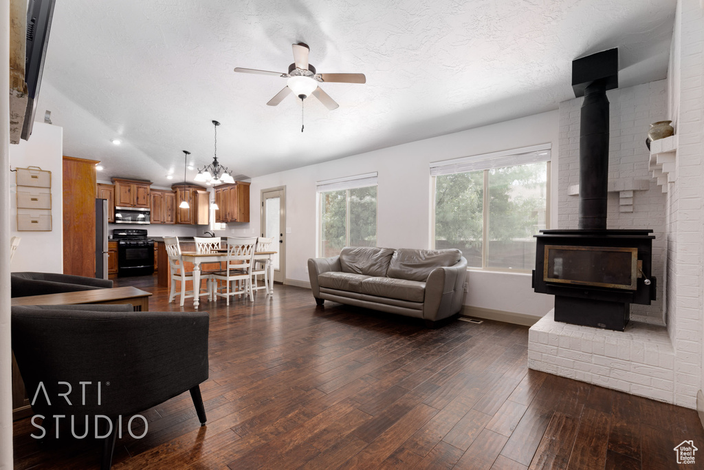 Living room with a wood stove, ceiling fan with notable chandelier, lofted ceiling, brick wall, and hardwood / wood-style flooring