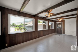 Unfurnished room featuring plenty of natural light, wooden walls, a notable chandelier, and beam ceiling