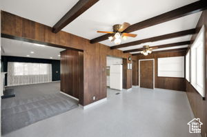 Empty room with wood walls, ceiling fan, concrete floors, and beam ceiling