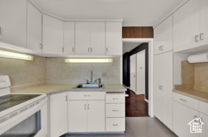 Kitchen featuring stove, tasteful backsplash, sink, white cabinetry, and hardwood / wood-style flooring