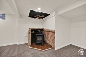 Unfurnished living room with a wood stove, beamed ceiling, carpet, and ceiling fan