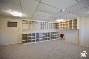 Basement with a drop ceiling, carpet floors, and an AC wall unit