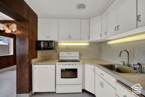 Kitchen with extractor fan, white appliances, sink, backsplash, and white cabinetry