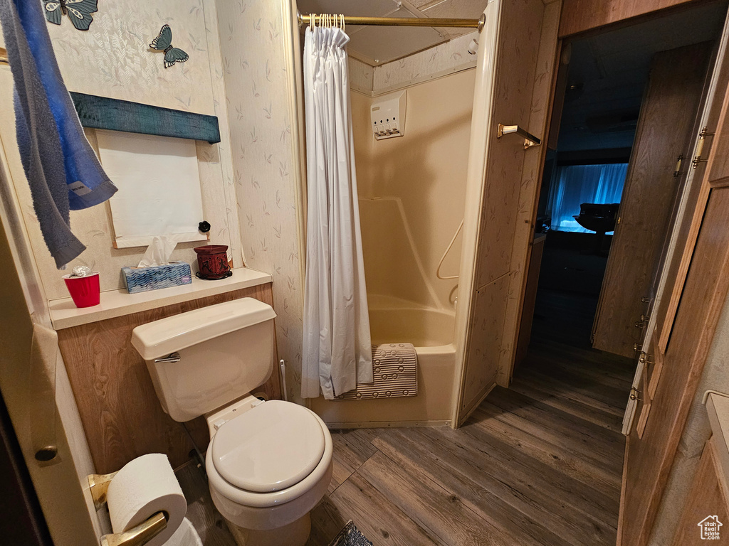 Bathroom featuring hardwood / wood-style flooring, toilet, and shower / tub combo with curtain