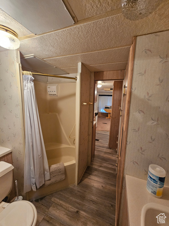 Full bathroom featuring toilet, hardwood / wood-style floors, a textured ceiling, and shower / tub combo