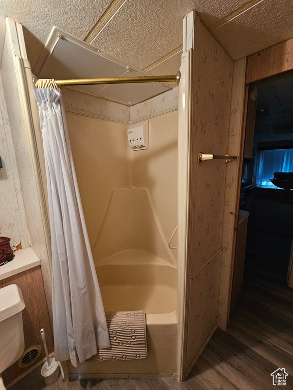 Bathroom featuring toilet, wood-type flooring, shower / bath combo, and a textured ceiling