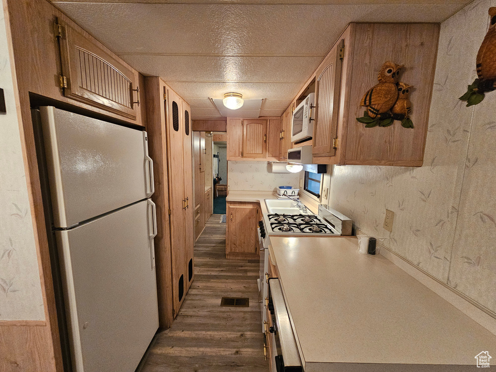 Kitchen with white appliances, a textured ceiling, dark wood-type flooring, light brown cabinetry, and sink