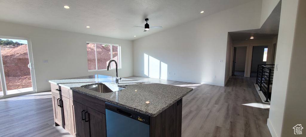 Kitchen featuring light hardwood / wood-style floors, light stone countertops, a center island with sink, stainless steel dishwasher, and sink