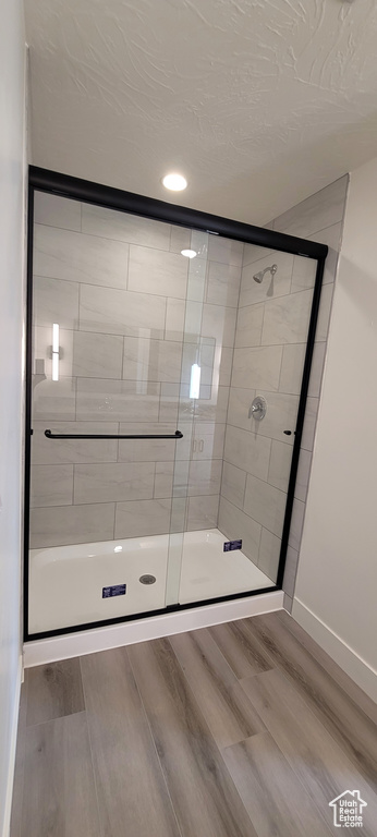 Bathroom featuring a textured ceiling, a shower with door, and hardwood / wood-style floors