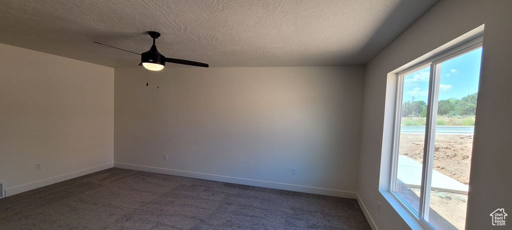 Empty room featuring dark colored carpet, a textured ceiling, and ceiling fan