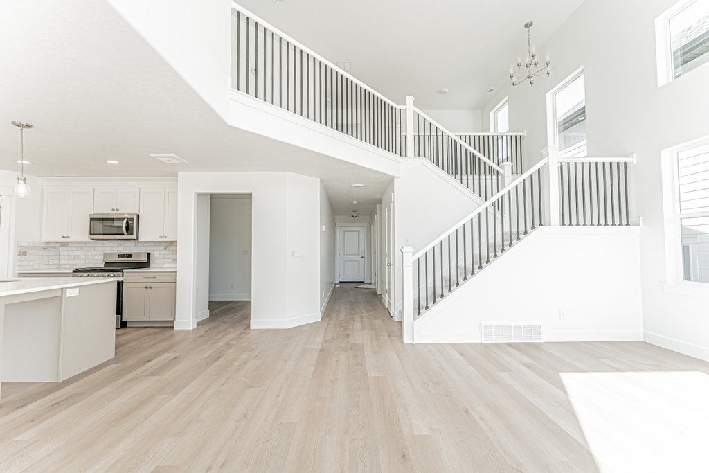 Unfurnished living room with light wood-style floors, a high ceiling, stairway, baseboards, and a chandelier