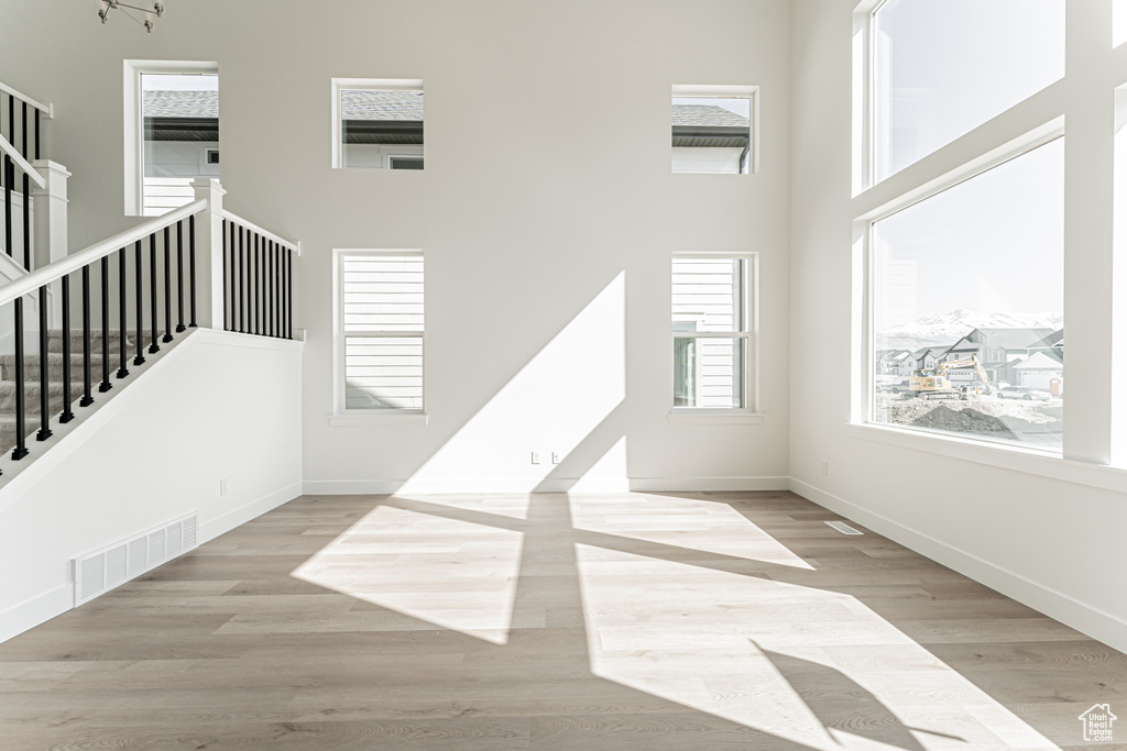 Unfurnished living room featuring stairs, wood finished floors, a towering ceiling, and baseboards