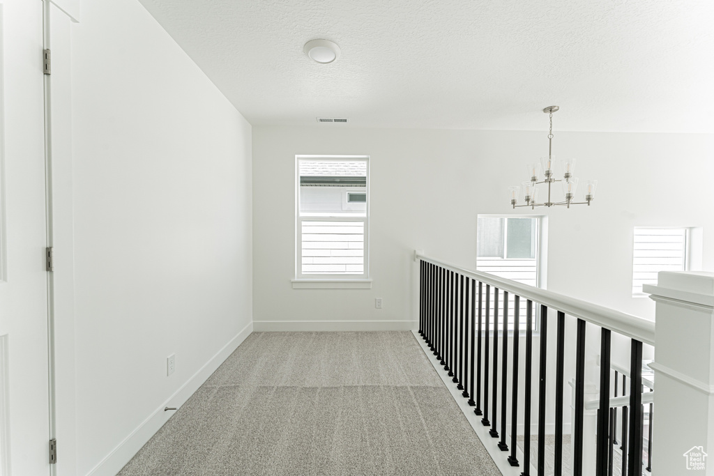 Hall with a chandelier, baseboards, carpet flooring, a textured ceiling, and an upstairs landing