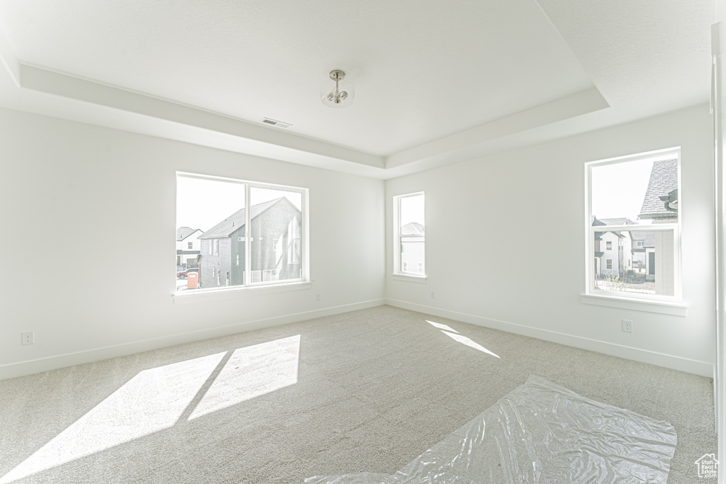 Carpeted empty room featuring a tray ceiling and baseboards