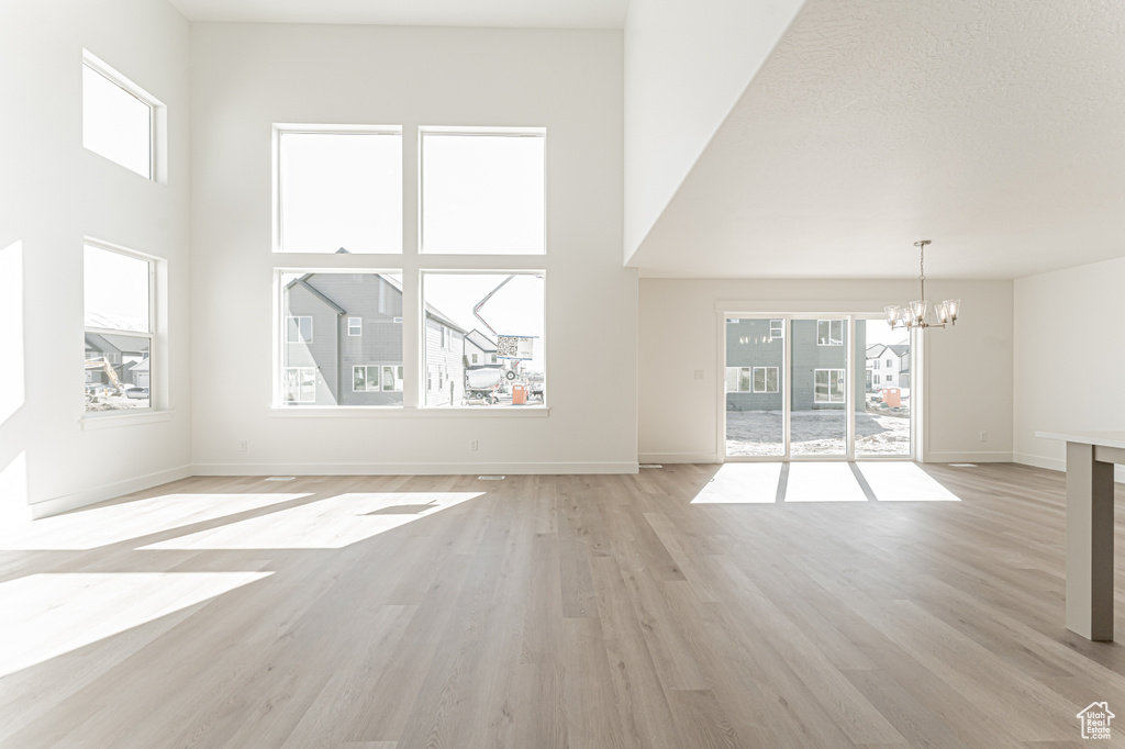 Unfurnished living room with a chandelier, plenty of natural light, light wood-style flooring, a towering ceiling, and baseboards