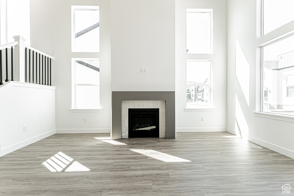 Unfurnished living room with a tiled fireplace, baseboards, wood finished floors, and a towering ceiling