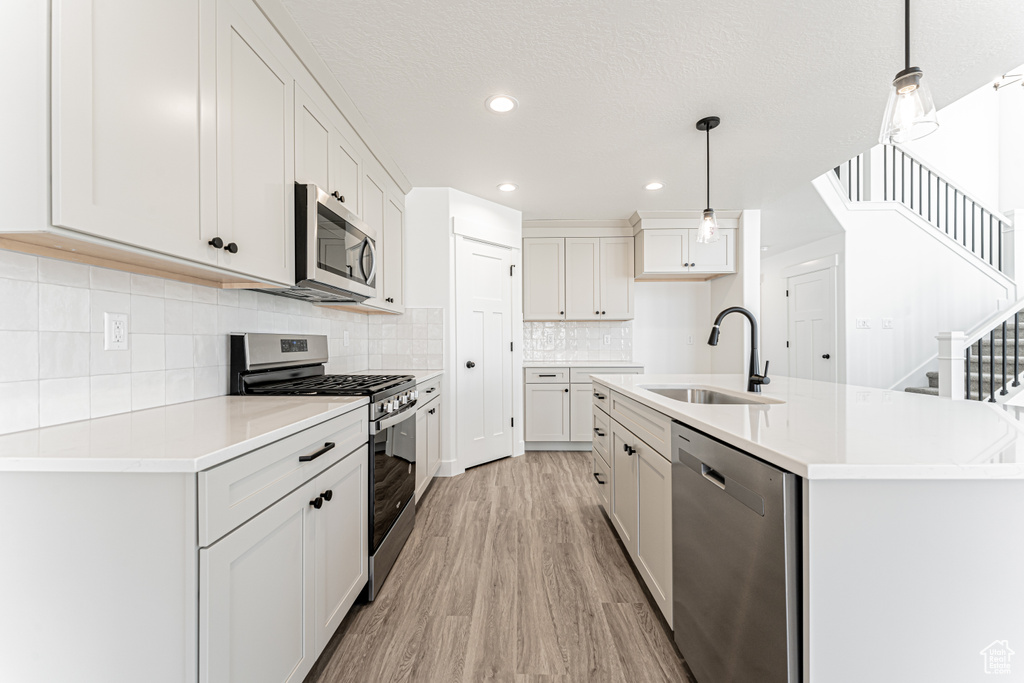Kitchen featuring tasteful backsplash, hanging light fixtures, a sink, appliances with stainless steel finishes, and light wood-style flooring
