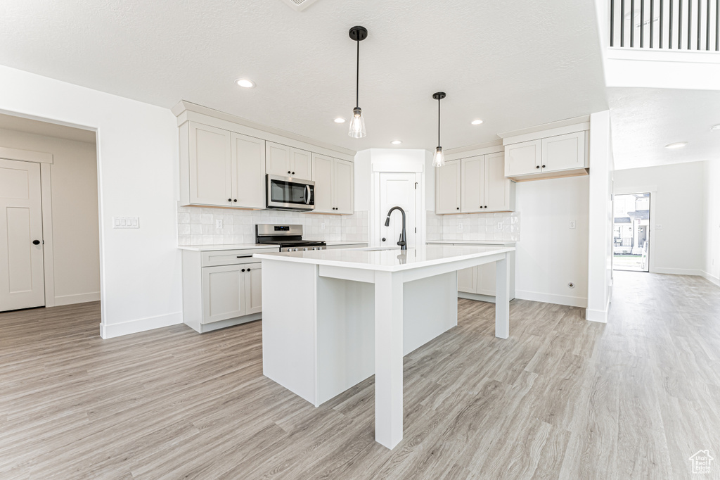 Kitchen featuring tasteful backsplash, light countertops, light wood-style flooring, and stainless steel appliances