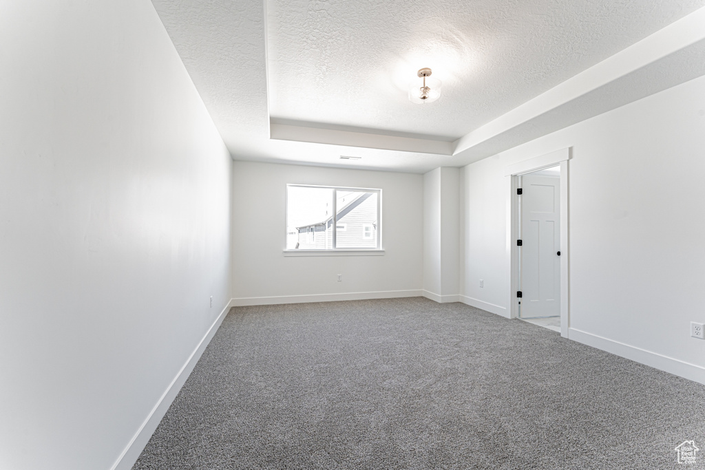 Spare room featuring a textured ceiling, visible vents, light carpet, a raised ceiling, and baseboards