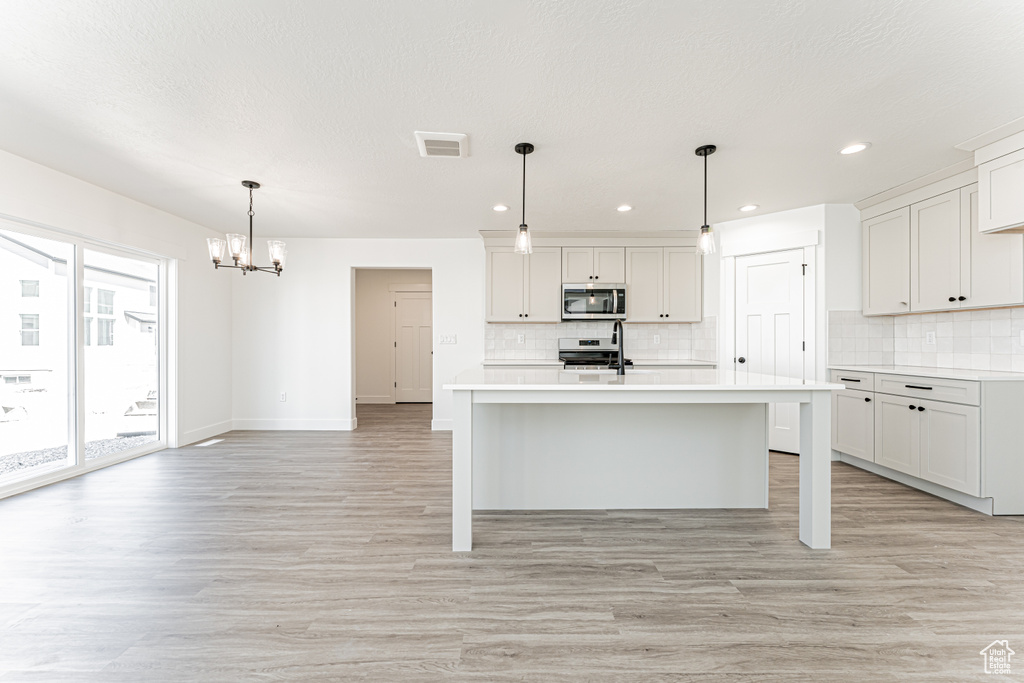 Kitchen featuring light wood-style flooring, tasteful backsplash, light countertops, stainless steel appliances, and a notable chandelier