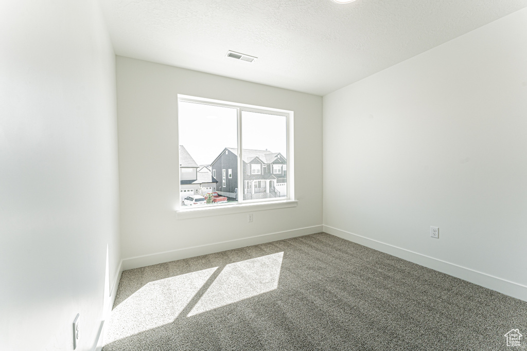 Empty room featuring carpet, visible vents, baseboards, and a textured ceiling
