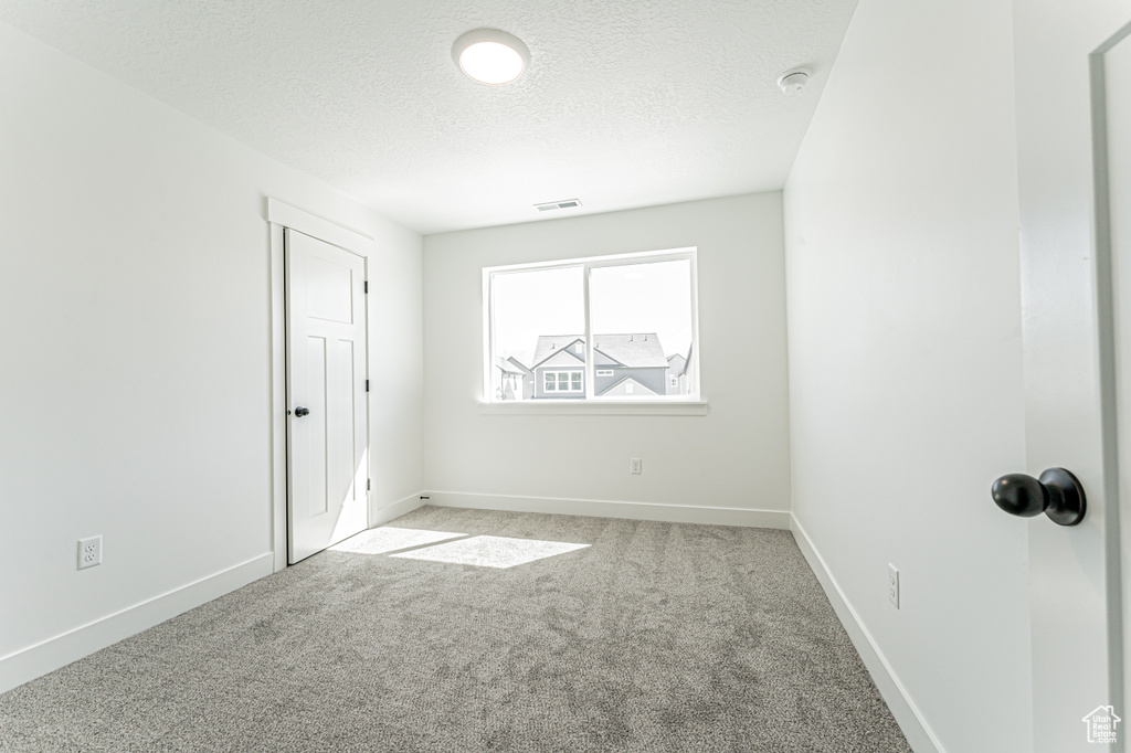Spare room featuring baseboards, visible vents, light colored carpet, and a textured ceiling