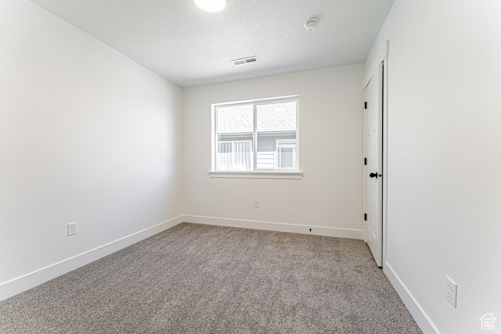 Spare room with a textured ceiling, baseboards, carpet, and visible vents