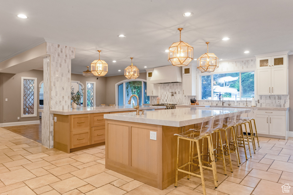 Kitchen with light tile patterned floors, premium range hood, decorative backsplash, decorative light fixtures, and a large island with sink