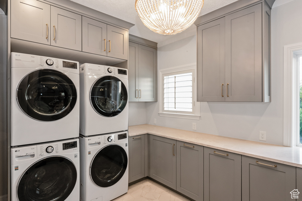 Laundry room featuring light tile patterned floors, an inviting chandelier, washer and dryer, cabinets, and stacked washer and clothes dryer