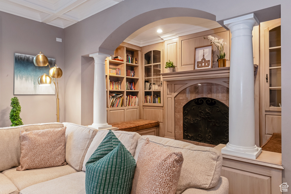 Living room featuring a tiled fireplace, crown molding, coffered ceiling, and decorative columns