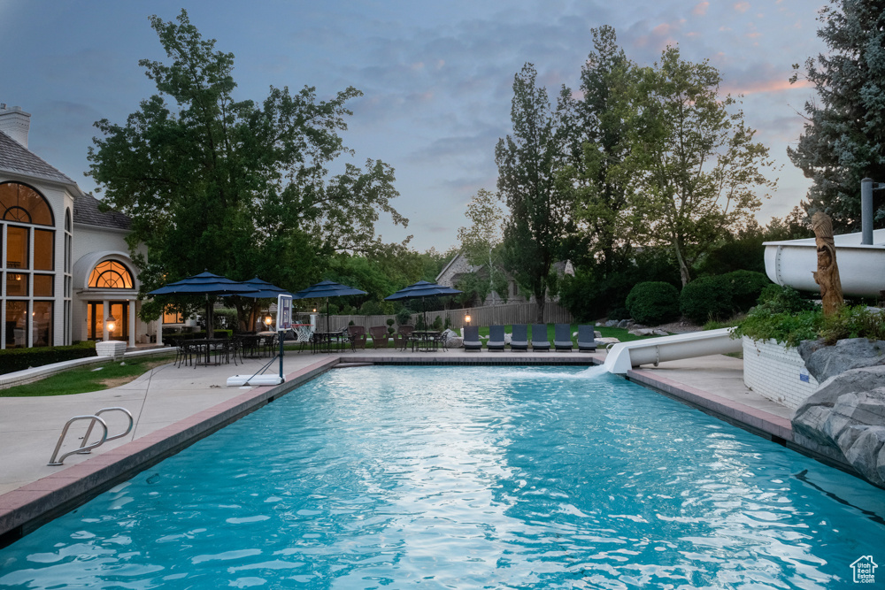 Pool at dusk featuring a water slide and a patio