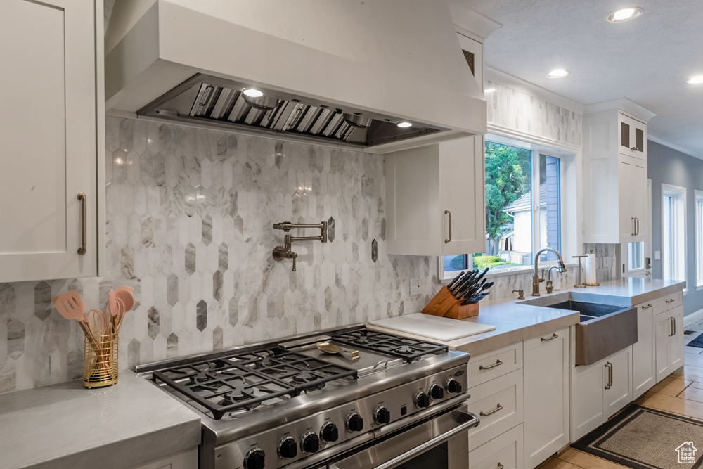 Kitchen featuring range with two ovens, tasteful backsplash, white cabinets, light tile patterned floors, and custom exhaust hood