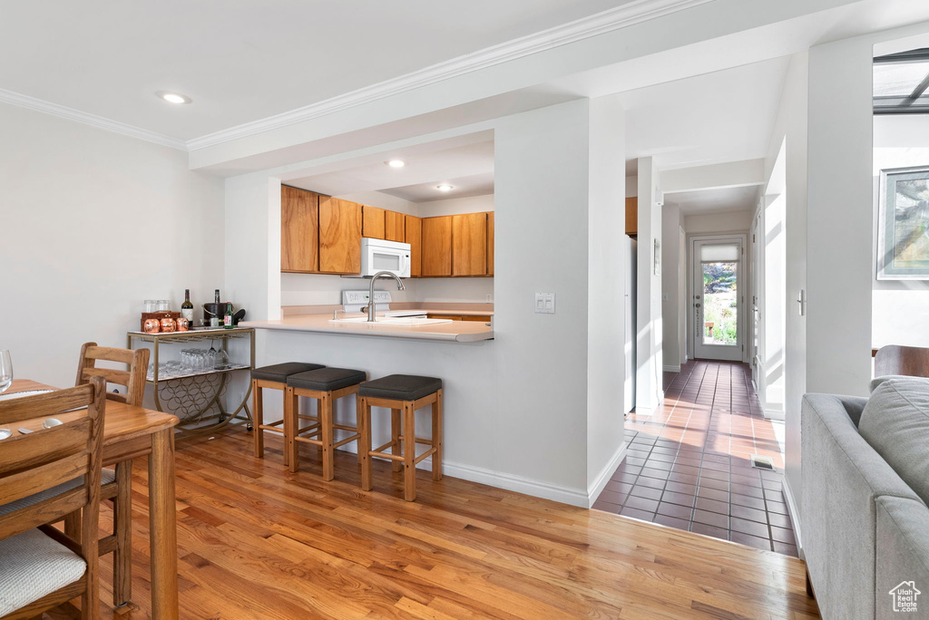 Kitchen featuring white appliances, light wood-type flooring, kitchen peninsula, a kitchen bar, and ornamental molding